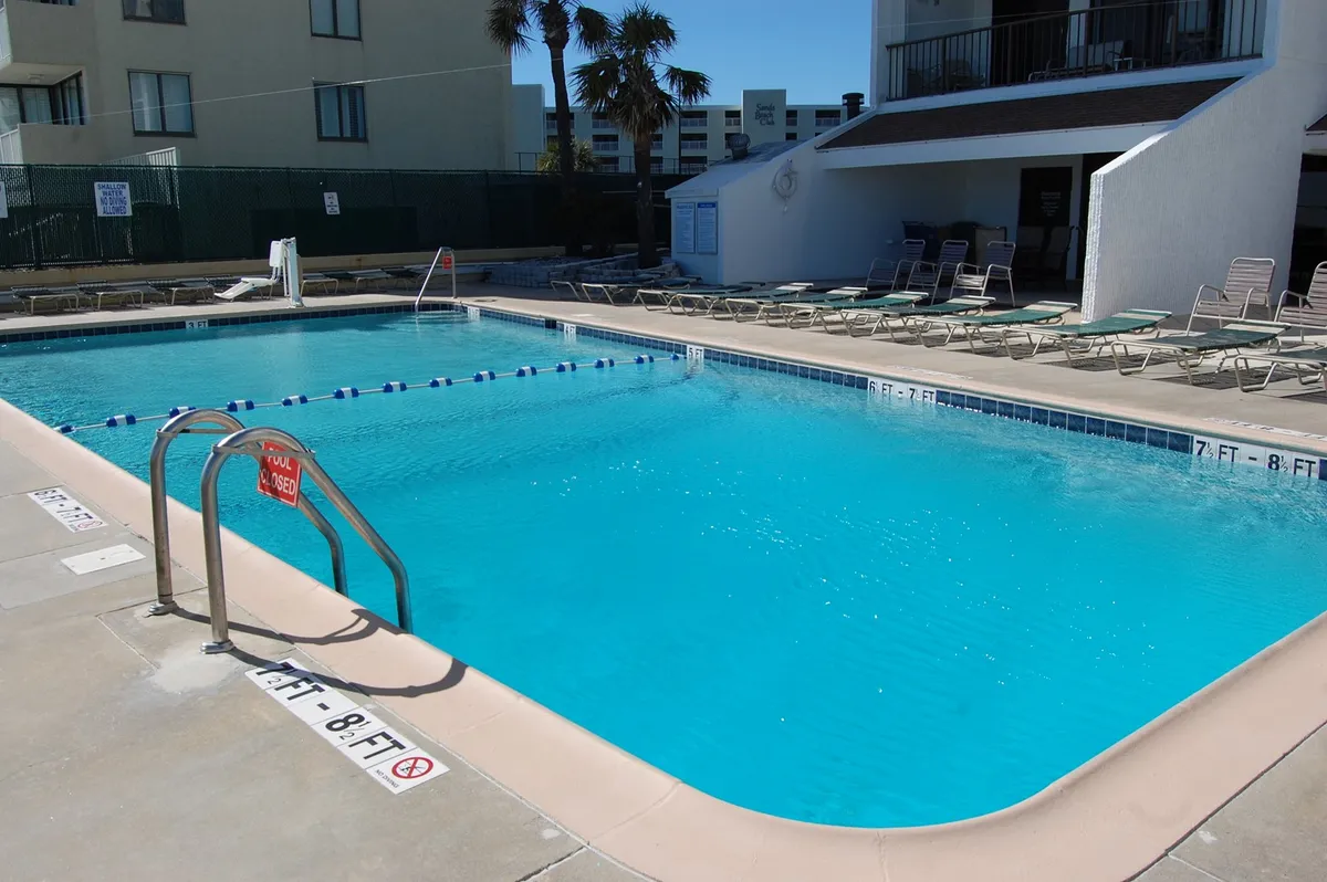 The image captures a sparkling pool area with inviting lounge chairs, framed by swaying palm trees and the condominium’s exterior. The atmosphere is tranquil yet social, suggesting both relaxation and community gatherings.