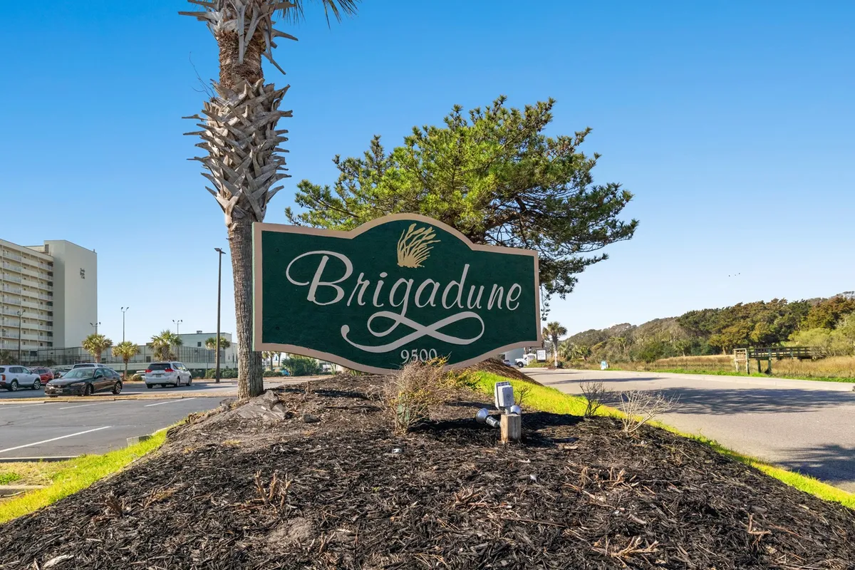 The image features the Brigadune property sign surrounded by lush palm trees and greenery, giving a welcoming sense of arrival and highlighting the property's inviting exterior. It establishes a connection to the location and offers guests a first impression of where their group adventure begins.