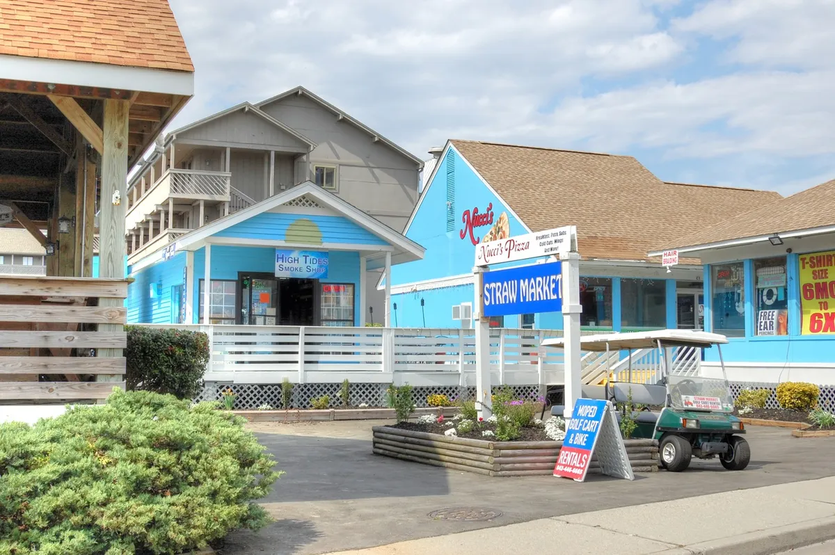 The image showcases a cheerful row of colorful buildings with visible signage and a golf cart parked nearby, hinting at local shopping, dining, and easy exploration options. The mood is inviting and bright, suggesting fun days discovering nearby attractions.