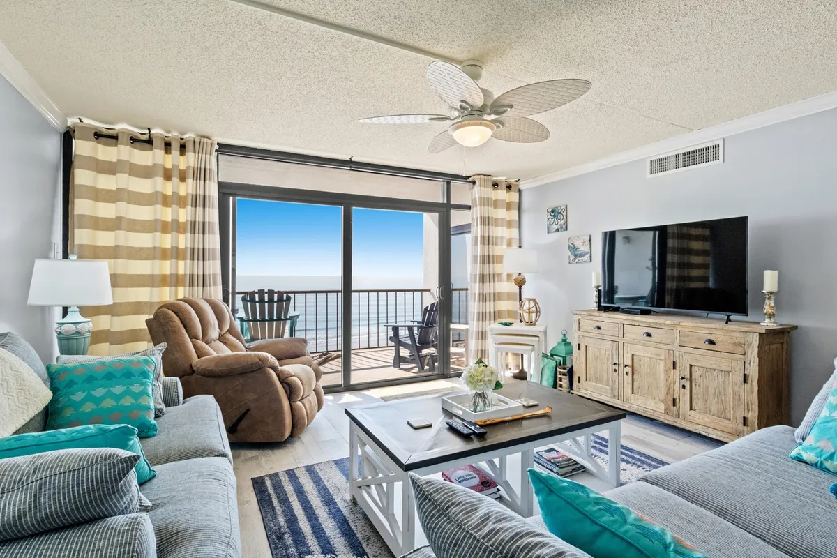 This image captures a bright, open living room with comfortable seating, a wooden coffee table, a television, and large windows framing panoramic ocean views. Decorative accents add a welcoming touch, and the scene radiates warmth and togetherness.