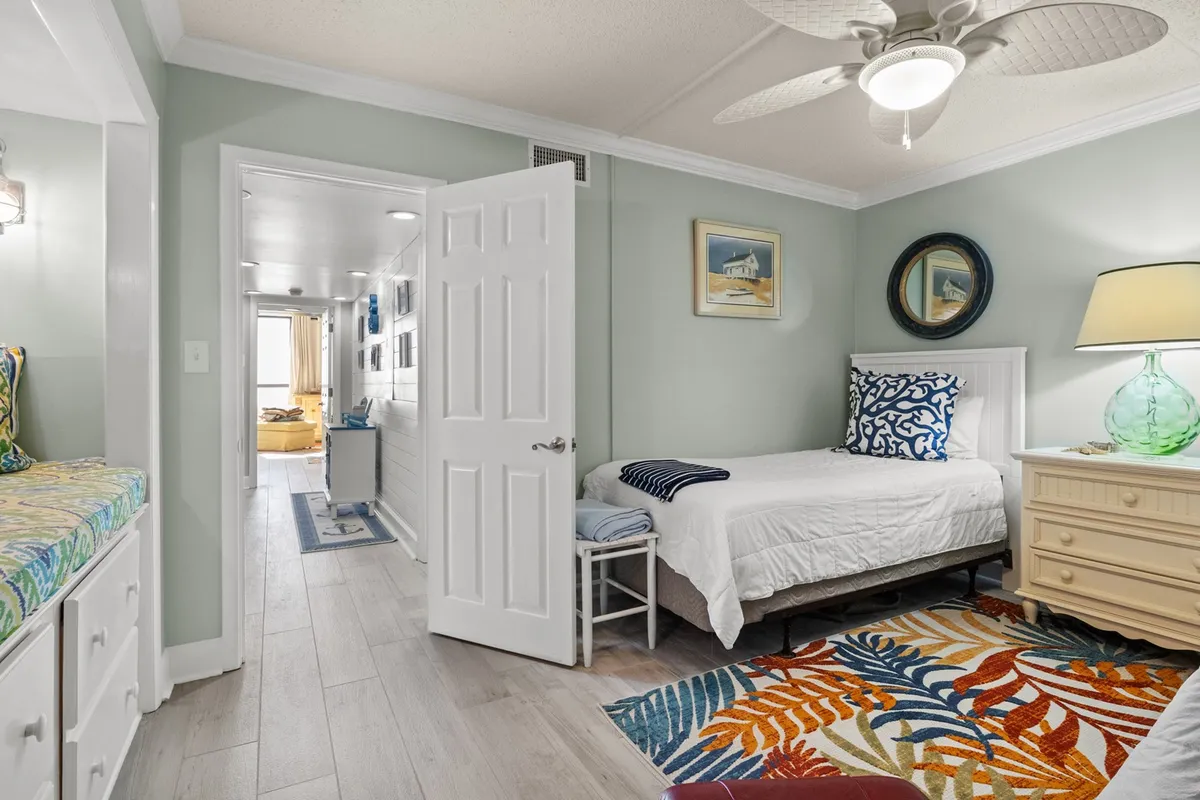 A cheerful and cozy bedroom with a bed adorned in decorative pillows, a vibrant area rug, and a green lamp, creating a playful and welcoming atmosphere ideal for relaxation or reading.